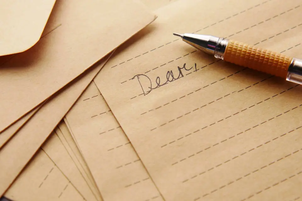 A handwritten letter on lined paper with kraft envelopes and a pen